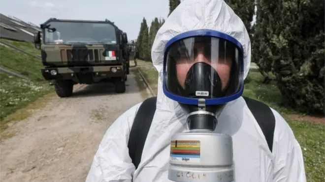 Seorang tentara Italia mengenakan alat pelindung diri saat memindahkan peti-peti jenazah dari truk militer ke kompleks permakaman di dekat Kota Milan, 27 Maret lalu.