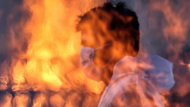 A municipal worker in Mumbai seen through the flames at a cremation