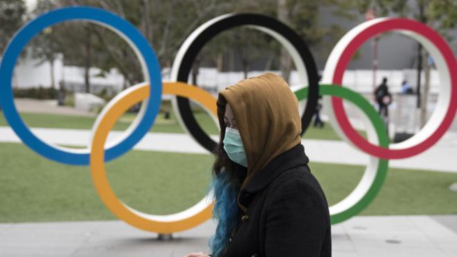 A woman in a face mask walks in front of the Olympic rings in Tokyo