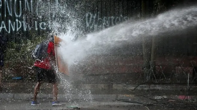Pengunjuk rasa menggunakan tameng buatan sendiri untuk menghadapi meriam air polisi huru-hara pada protes menentang pemerintah Chile di Santiago.