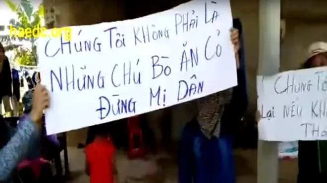 Người biểu tình giơ cao biểu ngữ trước cửa nhà trưởng thôn Cồn Sẻ