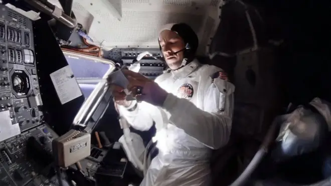 Apollo 13's commander Jim Lovell selects music on a portable tape player while Jack Swigert naps off to the right