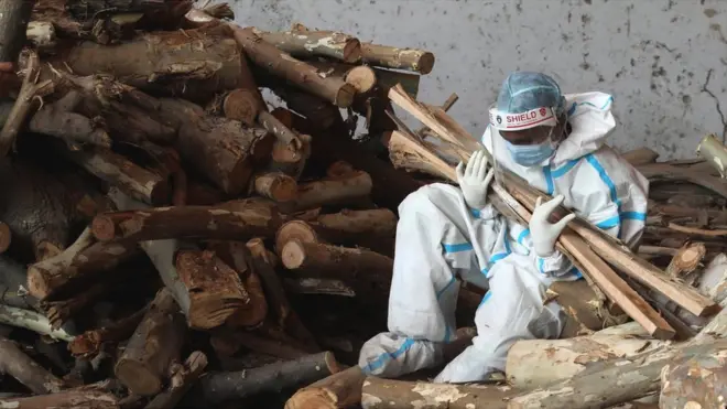 Image shows a relative of a Covid victim holding kindling for use in funeral pyres