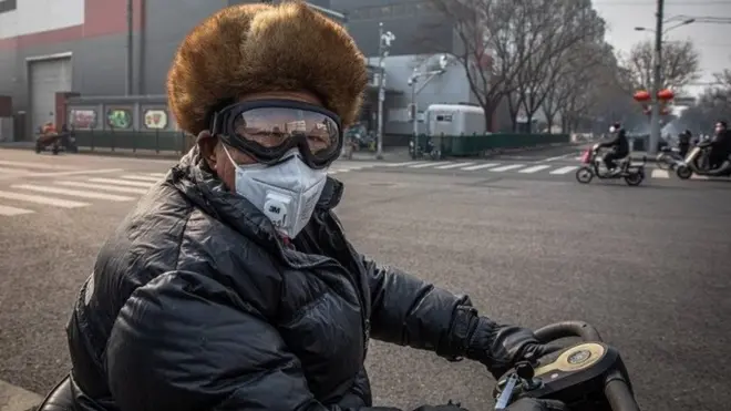 A man wearing a protective face mask and goggles rides on a vehicle in Beijing, China, 11 February 2020.