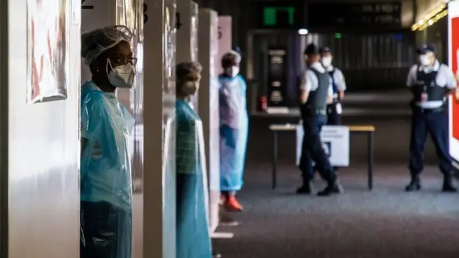 Health workers wearing protective gear wait for incoming travellers to arrive