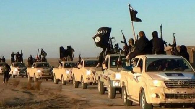 Undated photo shows militants of the Islamic State group hold up their weapons and wave its flags on their vehicles in a convoy on a road leading to Iraq, while riding in Raqqa city in Syria