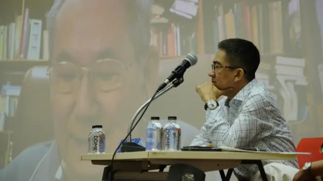 วรเจตน์ ภาคีรัตน์ นั่งอยู่หน้าจอที่มีภาพนิธิ เอียวศรีวงศ์