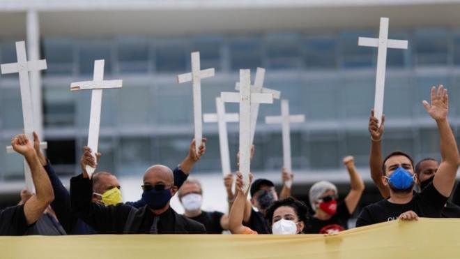Pessoas com máscara levantando cruzes em protesto