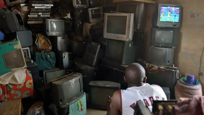 Man dey sit for in TV repairs shop dey watch TV