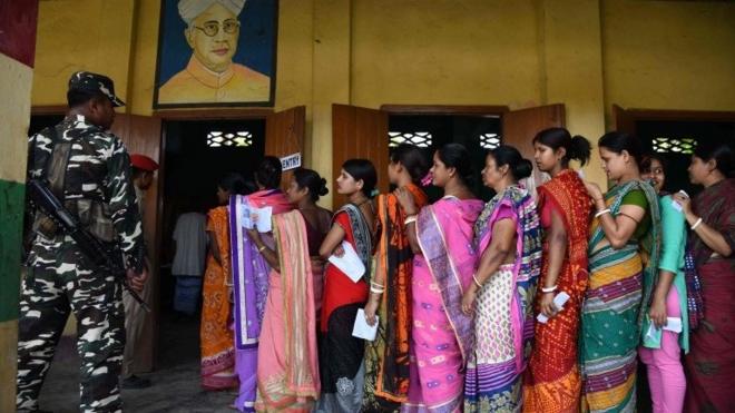 Indian voters stand in queue to cast their votes at a polling station as security personnel stand guard during India"s general election in Amoni village, some 150 kms from Guwahati, the capital city of India"s northeastern state of Assam on April 11, 2019.
