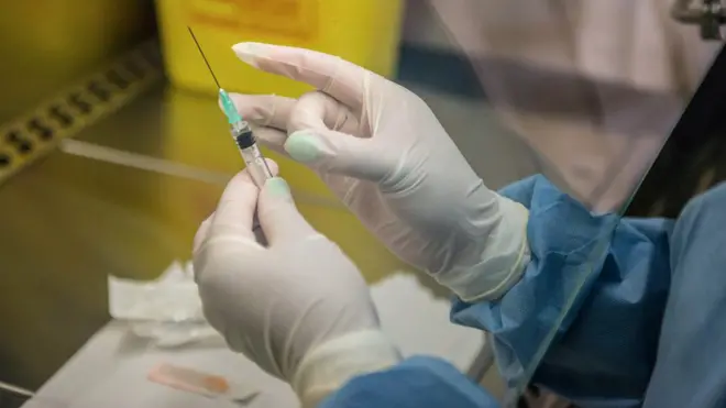 Hand wey wear glove dey hold syringe