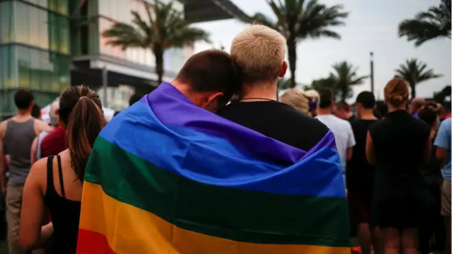 Men, draped in a rainbow flag, embrace ahead of a candle light vigil in memory of victims one day after a mass shooting at the Pulse gay night club in Orlando, Florida