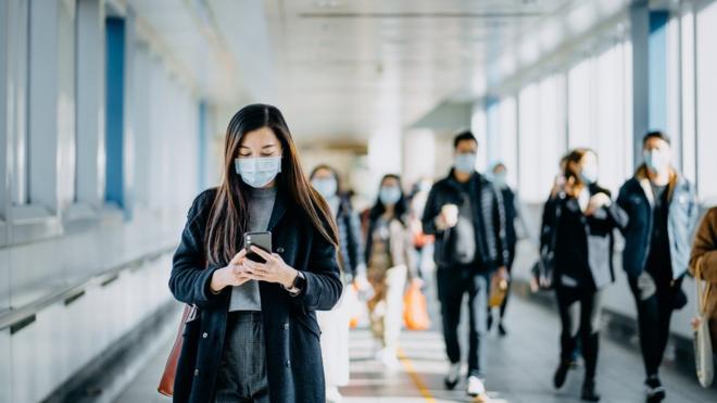 Mulher com máscara segura celular pertobolão da caixa dupla senaoutras pessoas