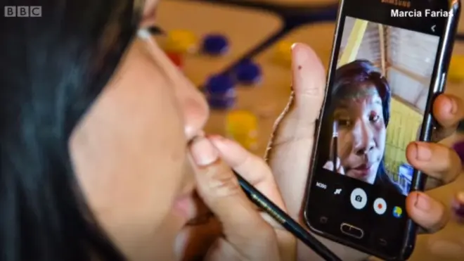 Mujer Kuikuru utilizando un celular para pintarse.