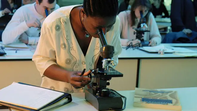 Femme noire travaillant avec un microscope.