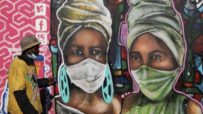 A man walks past a mural by Senzart911 that shows people wearing facemasks, as South Africa