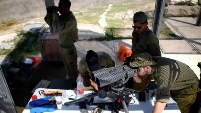 يقف جنود إسرئيليون على أهبة الاستعداد على الناحية الأخرى من الحدود