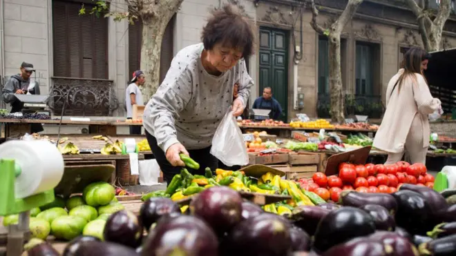 Una mujer compra verduras en un mercado en uruguay. 