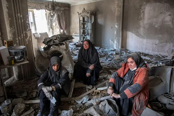 Três mulheres sentadas em uma casa que foi bombardeada no Irã