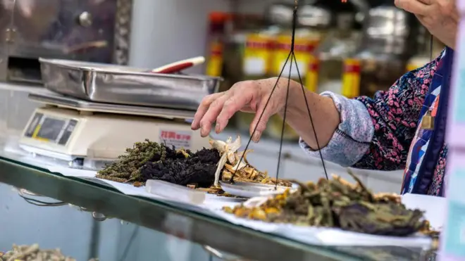 一位中醫醫師在藥局為顧客配製各種中藥。