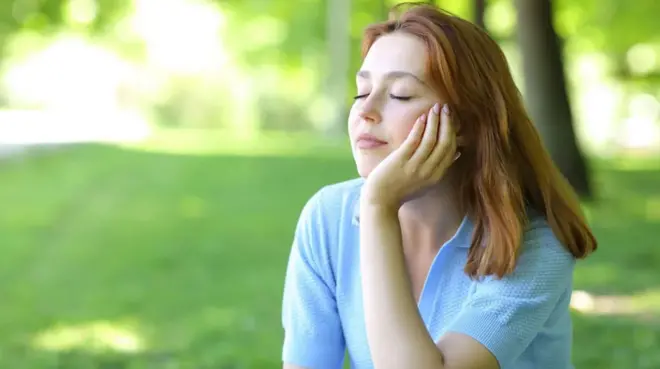 잔디밭에 앉아 눈을 감고 있는 여성 