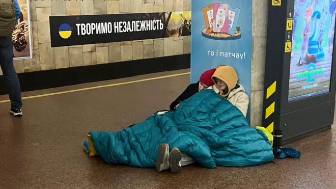 Підлітки сплять на підлозі станції метро в Києві - задньому фоні стіна метро з написом "Творимо незалежність"