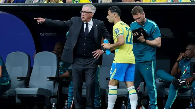 Ancelotti gesticula para Martinelli à beira do gramado; atrás, um assistente olha para uma prancheta.