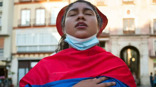 Mujer con la bandera de colombia en medio de una plaza española. 