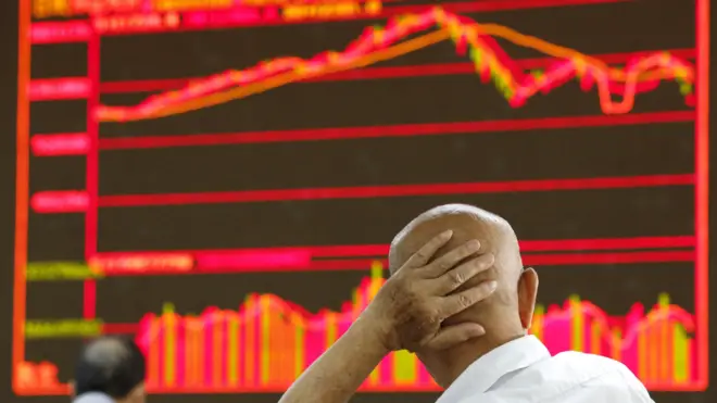 Una persona, de espaldas, se lleva la mano a la cabeza y de fondo se ve un panel con gráficos rojos