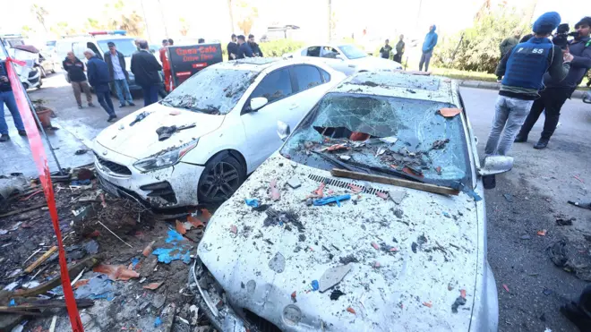 Two damaged cars covered in debris are pictured with crowds of people on the street in the background with rubble all around, after an Israeli missile attack on the coastal road in Sidon on Wednesday.