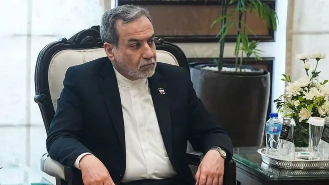 İranlı yetkili kravatsız takımla resmi bir odada oturuyor ve birini dinliyor.