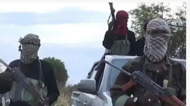 Awọn ọkunrin mẹta gbe ibọn dani, wọn bo oju ninu igbo ti won wa. Ọkan ninu won wa ninu ọkọ, awọn meji wa niwaju ọkọ naa.