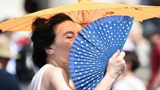 تصویر زنی که از گرما با بادبزن آسیای شرقی خود را باد می‌زند