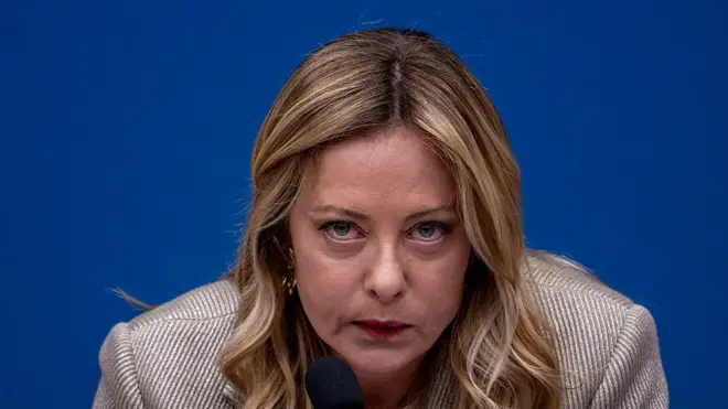 SArışın bir kadın kameraya bakıyor. Arkasında mavi bir fon var.