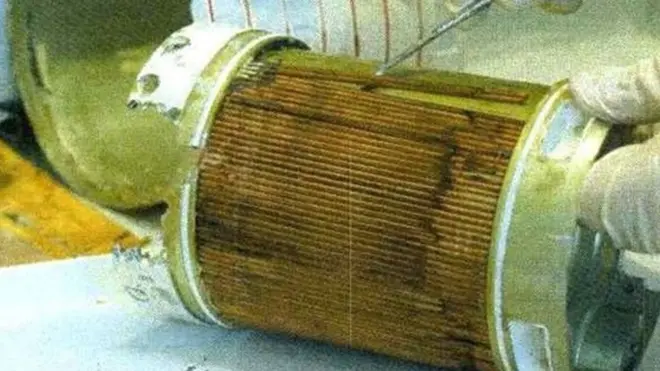 Крупний план циліндричного металевого елемента, розрізаного вздовж, із відкритою внутрішньою частиною. Всередині видно густо складену коричневу гофровану вставку — фільтрувальний матеріал, покритий брудом і темними смугами. 