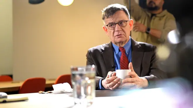 Андрей Ланьков сидит с чашкой во время съемки