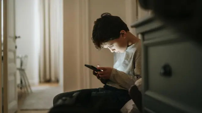 Menino olhando concentrado para o celular em casa