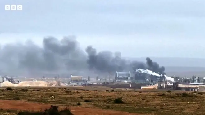 野原で黒煙の上がる施設