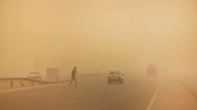 Ọkùnrin kan fẹ́ sọdá ojú pópó, àwọn ọkọ̀ ń kọjá, kùrukùru bo ojú ọjọ́