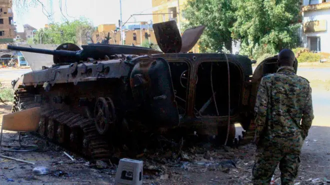 أحد المقاتلين يقف أمام مركبة عسكرية محترقة في شمال الخرطوم