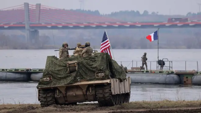 Amerykańscy żołnierze w pojeździe inżynieryjnym obserwują francuski prom wojskowy przeprawiający się przez Wisłę podczas ćwiczeń NATO Dragon 24 w pobliżu Gniewu w Polsce, 4 marca 2024 roku.
