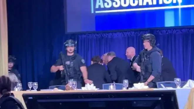 Perezida Donald Trump atwawe n'abashinzwe umutekano agenda yunamye, mu gihe abandi bamwe bahagaze, inyuma hari gitambaro kinini cy'ubururu.