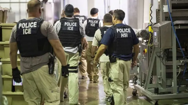 ብረት ዝዓጠቑ ሓያለ ሰብ መዚ ኢሚግረሽን፡ ፖሊስ ኣይስ ዝብል ዝተጻሕፎ ድርዒ ተኸዲኖም ኣብ ውሽጢ ሓደ ማእከል እናኸዱ፡ ብእድሕሪኦም ይራኣዩ