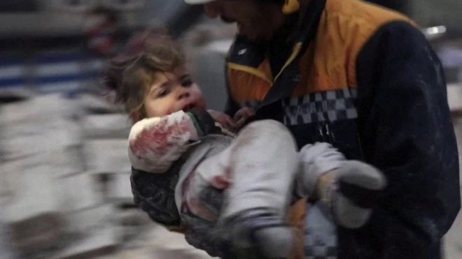 A rescuer carries a Syrian toddler, Raghad Ismail, away from the rubble of a building following an earthquake in rebel-held Azaz, Syria 