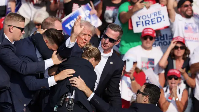  Trump, no palco onde realizou o comício, com a mão erguida e cercado por agentesrockets apostassegurança