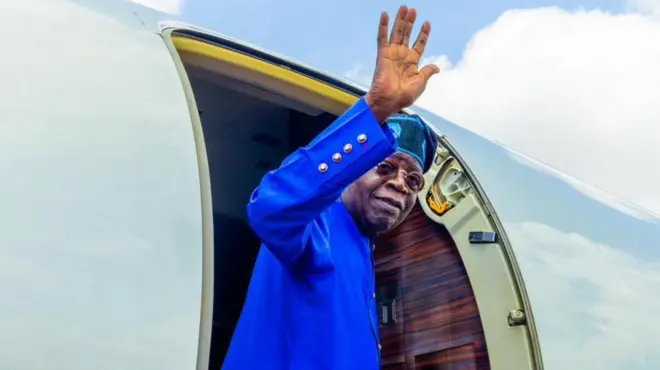 Aarẹ Tinubu n juwọ lẹnu ọna baluu kan.