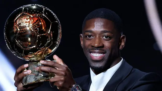 Мужчина держит в руках золотой мяч и улыбается в камеру