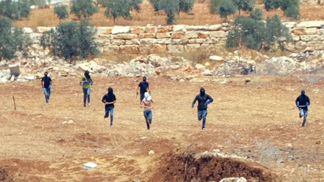 Seven masked figures run across a stretch of orange terrain towards the camera