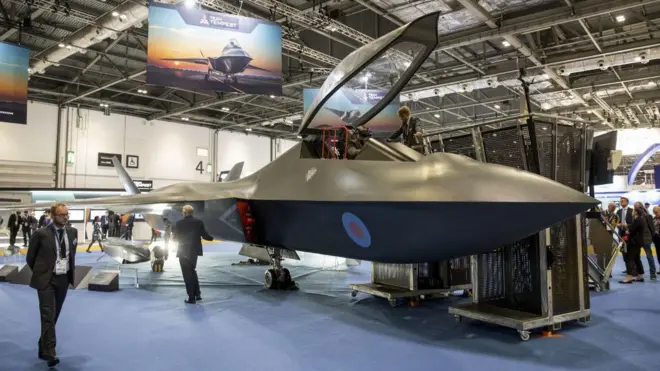 جت جنگی در فضای سرپوشیده نمایشگاه و شرکت‌کنندگان در کنارش