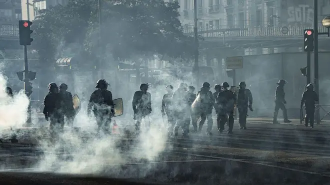 Полицейские в защитной форме в Париже переходят улицу в дыму от горящих мусорных баков